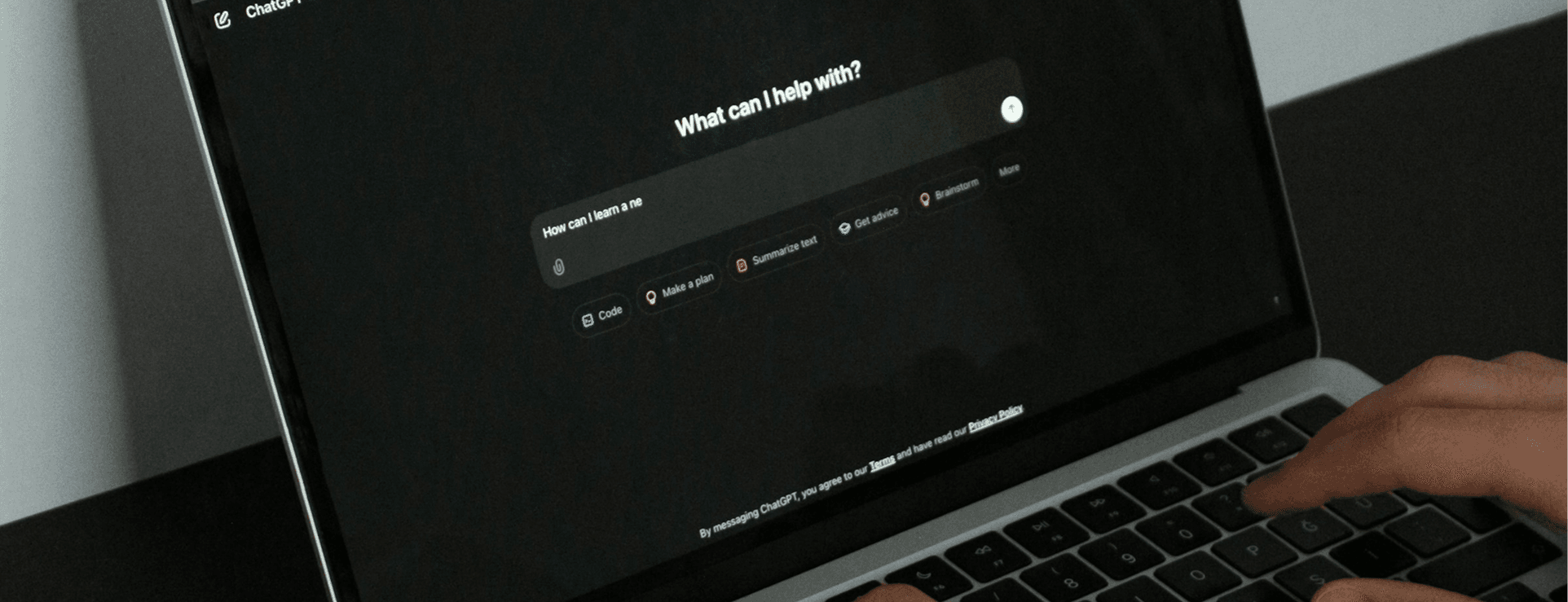 Jemand sitzt vor einem Laptop, auf dem ein KI-Chatbot im dunklen Modus läuft. Der Nutzer tippt auf der Tastatur.