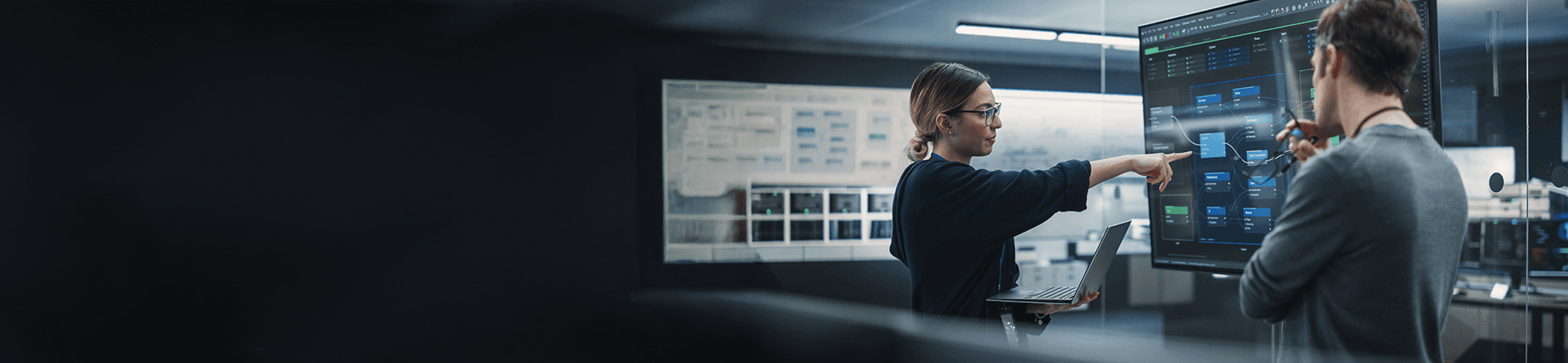 Frau mit Brille und Laptop zeigt auf ein großes Datendiagramm.