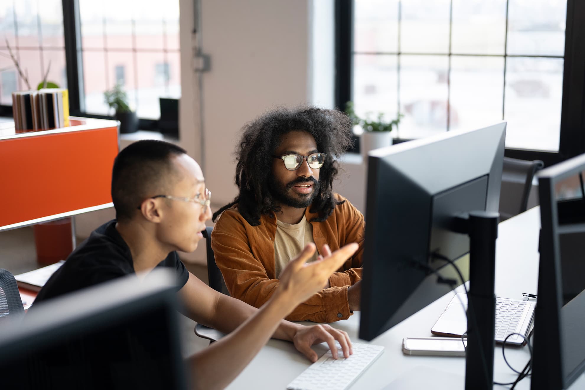 Zwei Männer mit Brille, die in einem Büro auf einen Monitor schauen und auf den Monitor zeigen